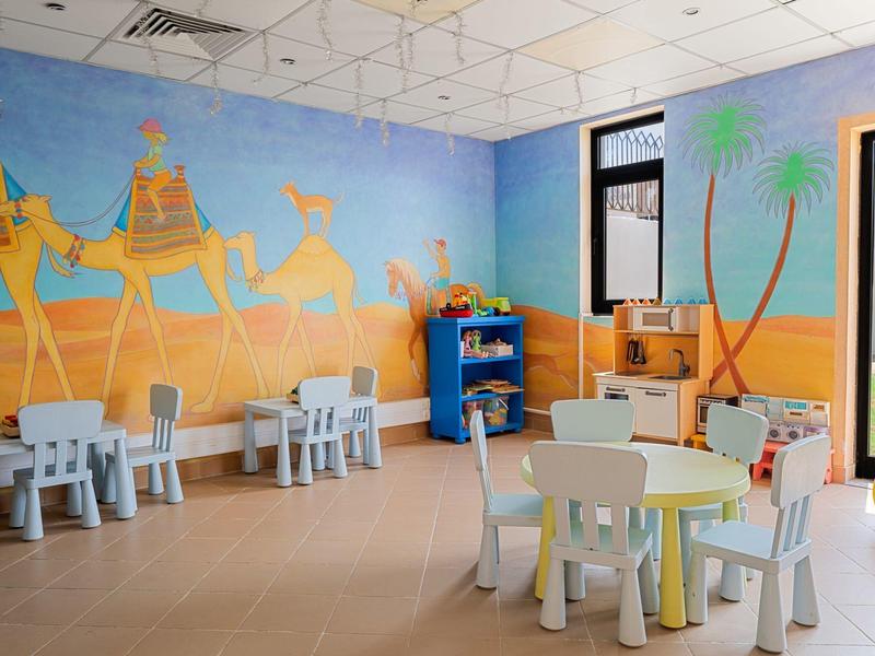 Children's room with tables, chairs, and a desert mural featuring camels.