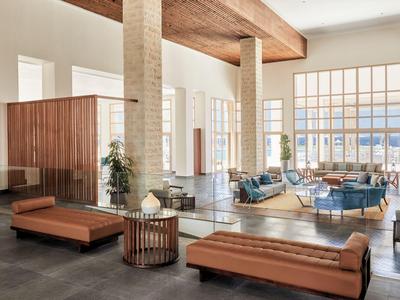 Moderner Hotellobby mit hohen Fenstern, braunen Sitzbänken und blauen Sofas in hellem Raum.