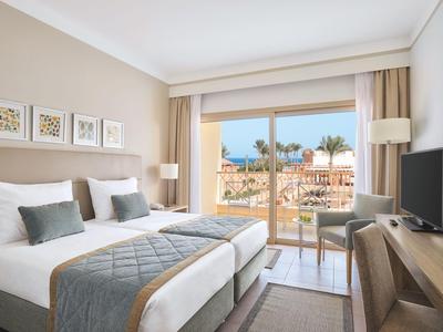 Modern eingerichtetes Hotelzimmer mit zwei Betten, Terrasse und Blick auf Palmen.