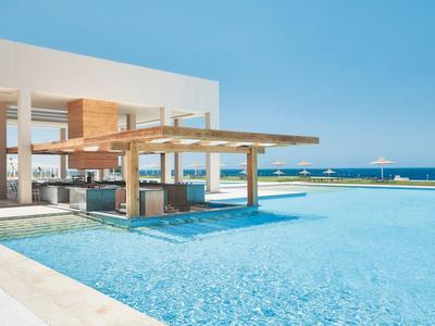 Moderner Poolbereich mit Swim-up-Bar und Blick auf das Meer bei klarem Himmel