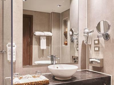 Bagno moderno in hotel con lavabo rotondo, grande specchio e accessori a parete.