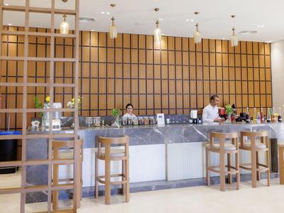 Nowoczesny bar hotelowy z drewnianymi stołkami i oświetlonym kontuarem, barmani podają napoje.