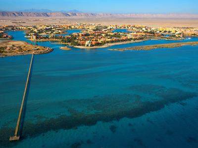 Aerial view of a coastal area with a long pier extending into clear blue water under a sunny sky.