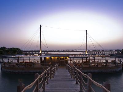 Wooden pier leads to floating restaurant with lights at twilight over calm water.