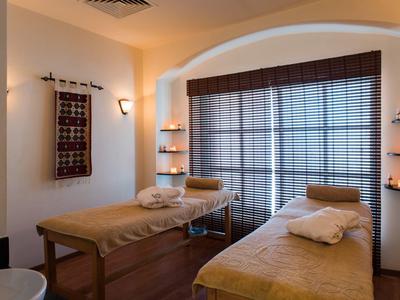 Cozy spa room with two massage beds, soft lighting, and large window blinds.