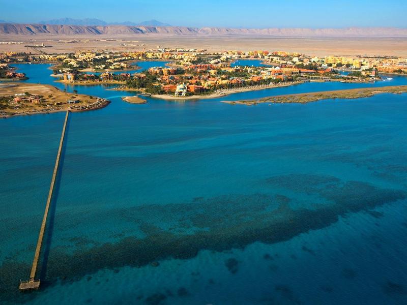 Aerial view of a coastal area with a long pier extending into clear blue water under a sunny sky.