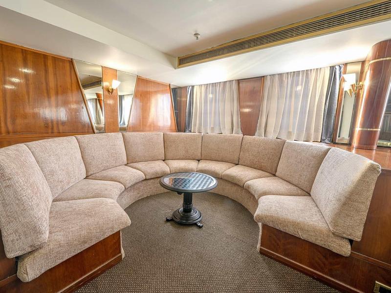 Curved beige sofa with a black round table in a wood-paneled room with large windows.