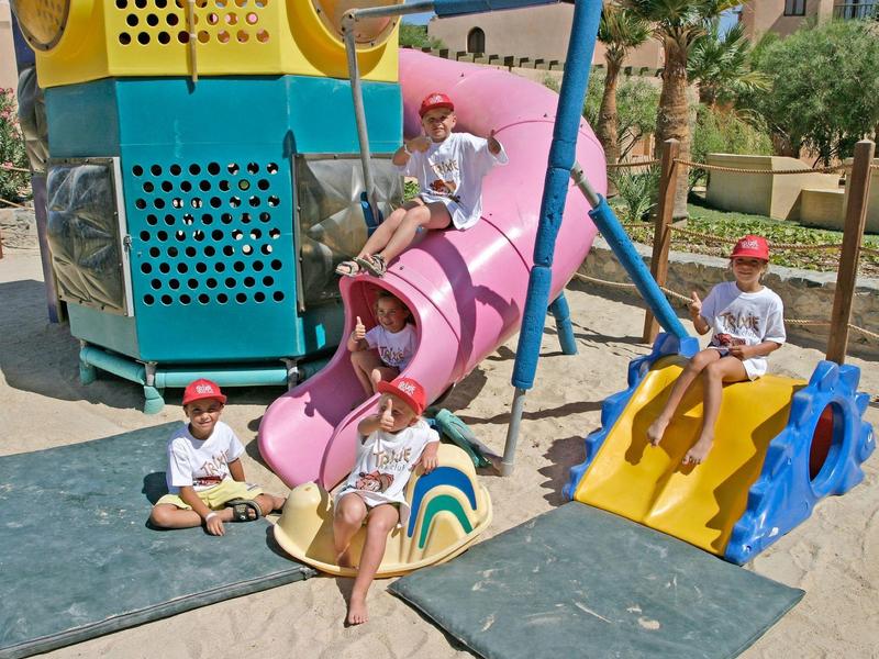 Niños juegan en parque infantil colorido con tobogán y estructura para escalar al aire libre.