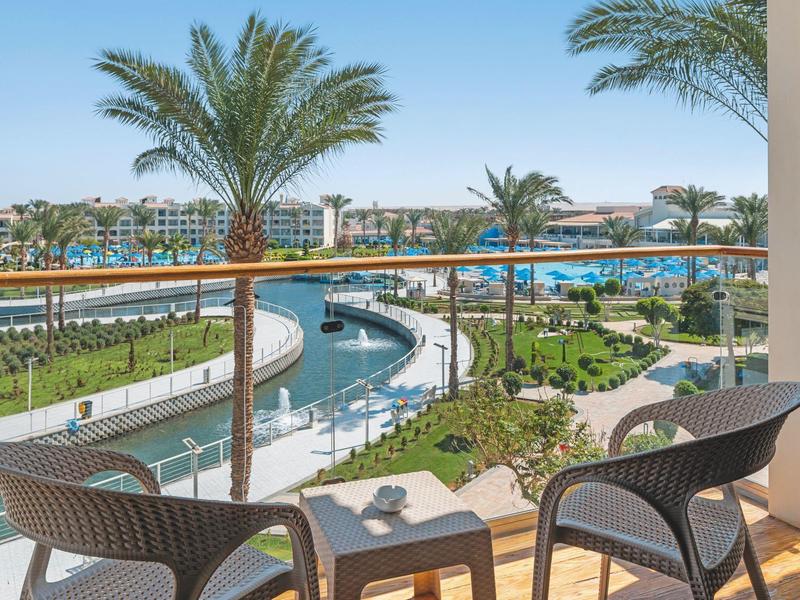 Balkon met stoelen en tafel met uitzicht op zwembad en palmbomen in een hotelresort.