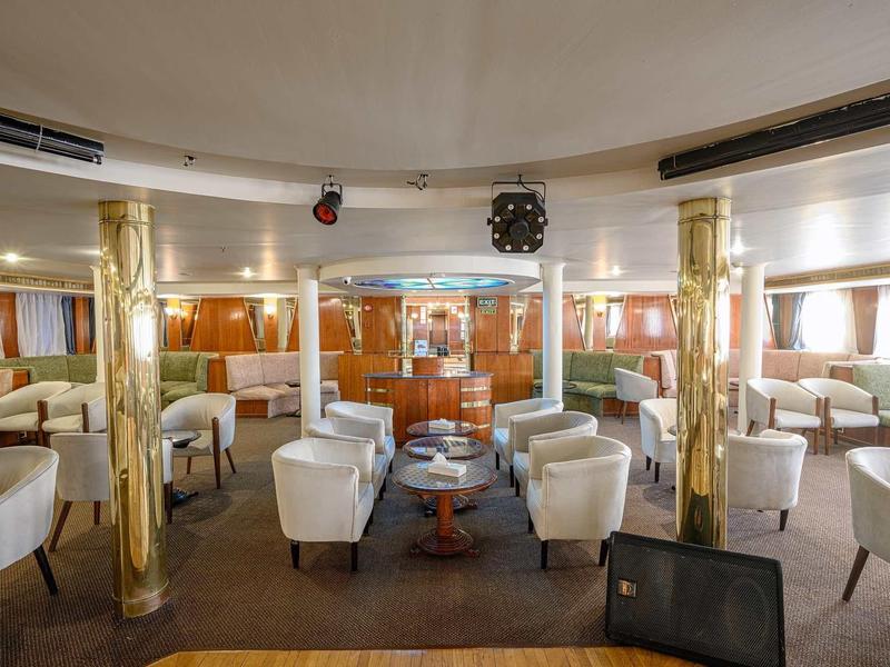 Großer heller Salon mit weißen Sesseln, goldenen Säulen und vielen Fenstern in einem Schiff.