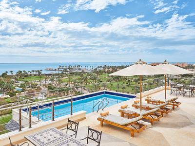 Terrasse avec piscine, chaises longues et vue sur la mer par ciel dégagé.
