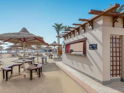 Beach area with sun umbrellas, tables, and a kiosk under a clear sky