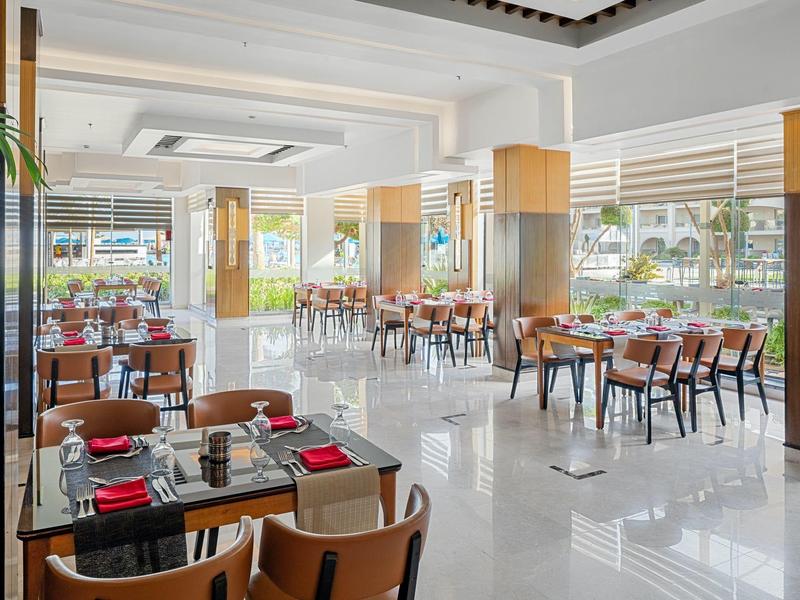 Lichte hotel eetruimte met glazen tafels, houten stoelen en grote ramen met uitzicht op buiten.