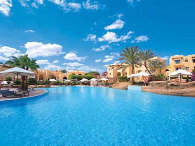 Grande piscina in un resort alberghiero soleggiato con lettini e ombrelloni sotto un cielo azzurro.