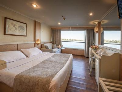 Chambre d'hôtel lumineuse avec grand lit, vue sur l'eau et mobilier en bois clair.