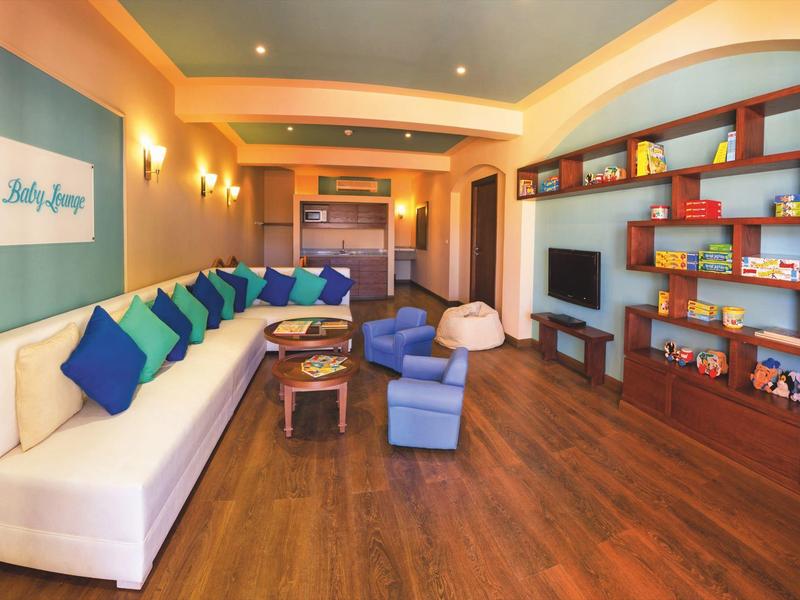 Sala de estar moderna con sofá blanco, cojines coloridos y estanterías de madera llenas de juegos de mesa.