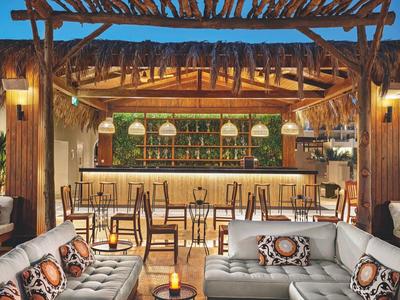 Gezellige buitenbar van hotel met houten pergola, zachte banken en warme verlichting bij schemering.