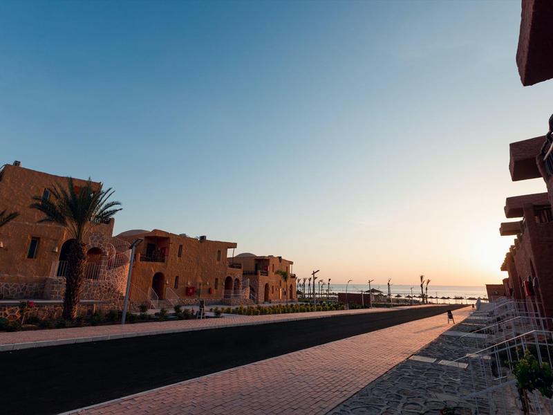 Sunset view of modern desert-style buildings along a paved street with palm trees.