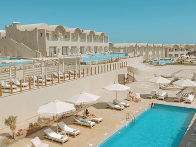 Hotel mit zwei Pools, Liegestühlen und Sonnenschirmen unter klarem Himmel.