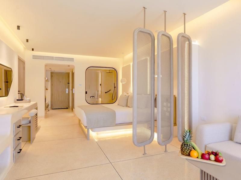 Chambre d'hôtel lumineuse et moderne avec lit double, luminaires suspendus uniques et fruits frais sur le comptoir.