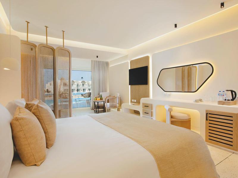 Chambre d'hôtel lumineuse avec grand lit, décor moderne, TV et vue sur balcon.