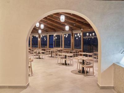 Área de restaurante moderno con techos de madera, mesas redondas y lámparas colgantes al anochecer.