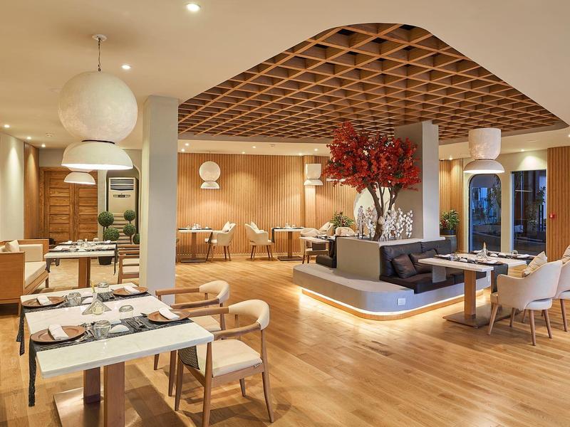 Área de comedor moderna en hotel con suelo de madera, muebles elegantes e iluminación suave.