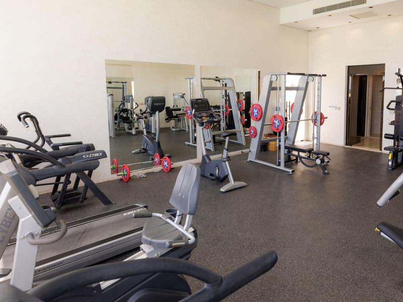 Gimnasio amplio con cintas de correr, equipos de entrenamiento y pared de espejos en interior luminoso.