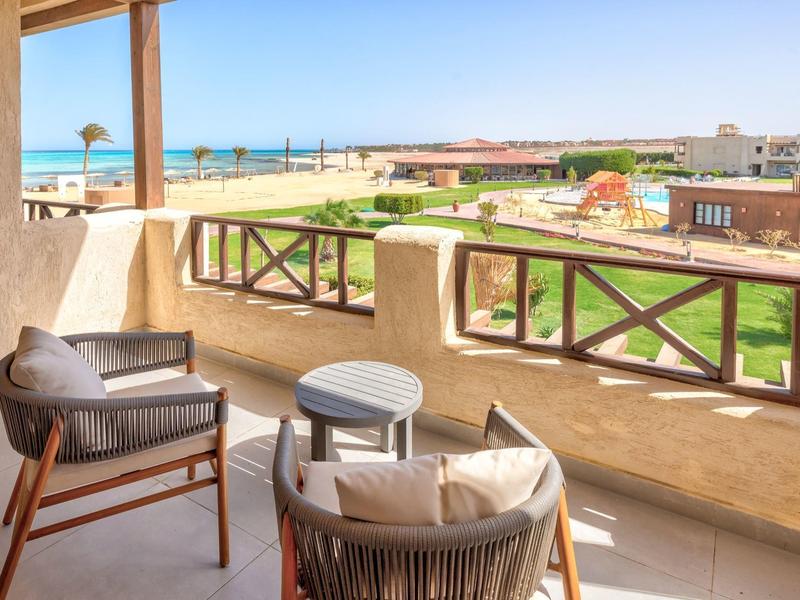 Balcón con sillas y mesa con vista a un jardín y el mar en el horizonte.