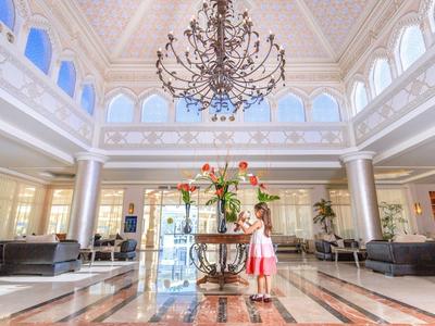 Amplio vestíbulo de hotel con mármol claro, candelabro y decoración floral en el centro.