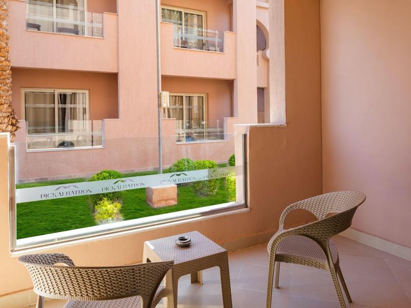 Balcón con dos sillas y mesa, vista a jardín cuidado y edificio del hotel.