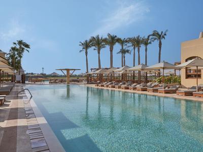 Grand piscine extérieure avec chaises longues et palmiers par une journée ensoleillée dans un complexe.