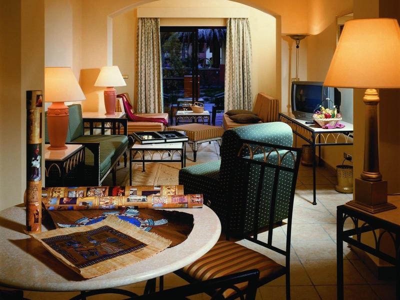 Przytulny salon hotelowy z dużym stołem, fotelem i ciepłym oświetleniem.