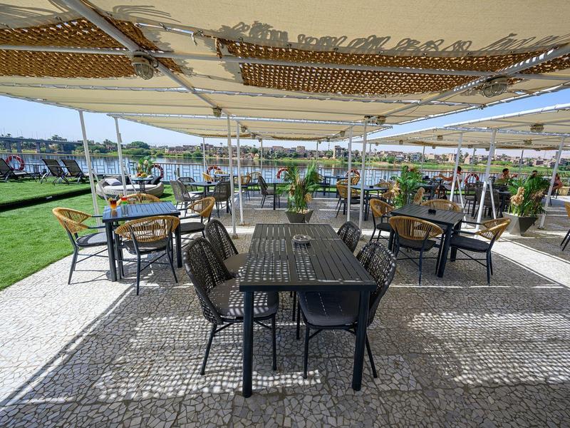 Zewnętrzny taras hotelowy z stołami i krzesłami pod dużym zadaszeniem.