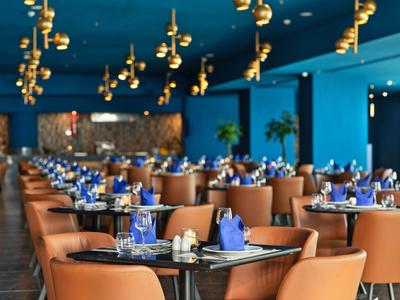 Moderní restaurace s hnědými koženými židlemi a zlatými závěsnými dekoracemi.