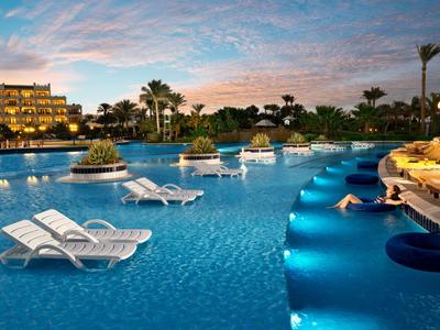 Area piscina dell'hotel serale con sedie a sdraio e illuminazione esterna soffusa.