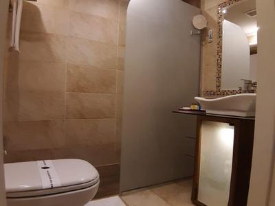 Kleines Badezimmer mit Wand-WC, frosted Duschwand, Waschbecken und beige Fliesen.