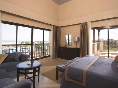 Camera d'hotel con letto matrimoniale, poltrone blu e balcone vista mare.