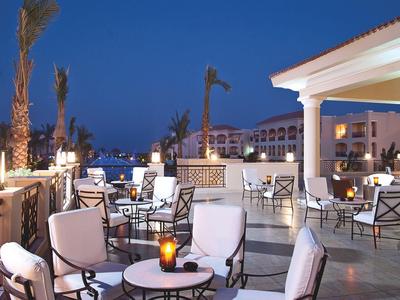 Hotel terrace at dusk with lit tables and chairs under a clear sky.