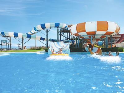 Water park with swimming pool and two colorful water slides under blue sky.