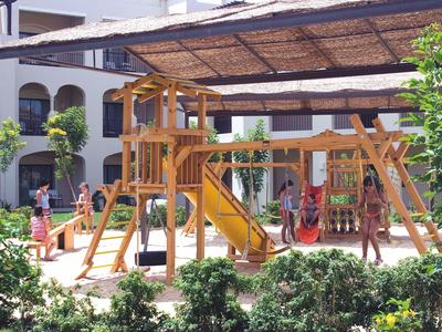 Children's playground with climbing frame and slide in front of a hotel building.