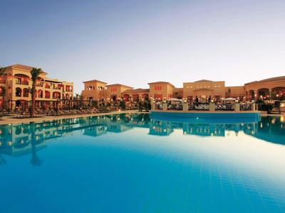 Ampia piscina azzurra che riflette un hotel in stile mediterraneo al tramonto.