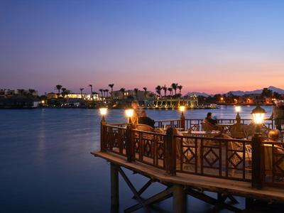 Terrasse romantique avec tables et bougies au bord d'un lac au coucher du soleil.