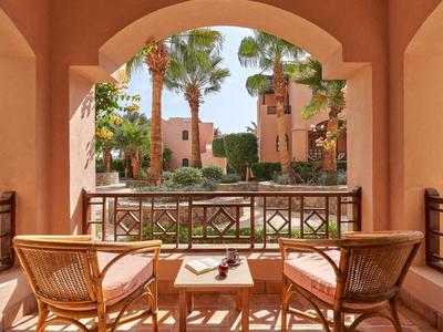 Balcon avec deux chaises en rotin et une table, vue sur un jardin paysager et des bâtiments.