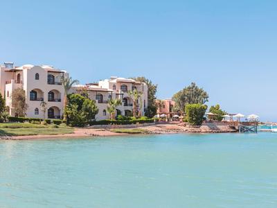 Complexe avec des bâtiments blancs au bord d’une mer turquoise calme sous un ciel dégagé.