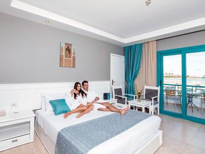 Habitación de hotel con cama, balcón y dos huéspedes relajándose de vacaciones.