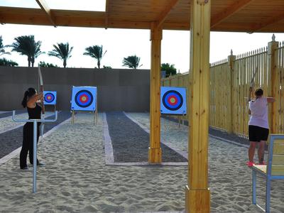 Two people practice archery on sandy ground with targets outdoors.