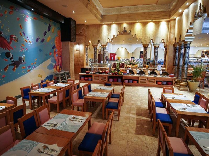 Restaurante moderno con mesas de madera, sillas azules, arte colorido en la pared y ambiente acogedor.