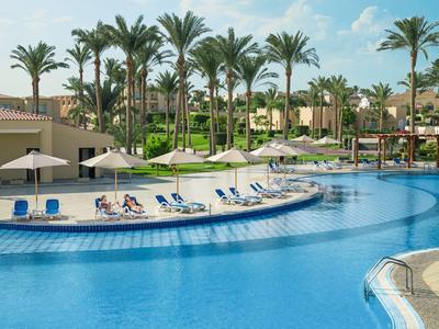 Grand piscine d'hôtel avec transats et palmiers sous un ciel dégagé.