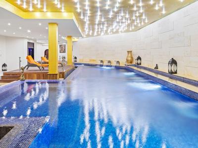 Modern indoor pool with lounge chairs, yellow columns, and ceiling lights in a hotel.